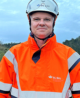 Porträt Jens Möller mit Warnkleidung, Aufsichtsperson der BG BAU.
    