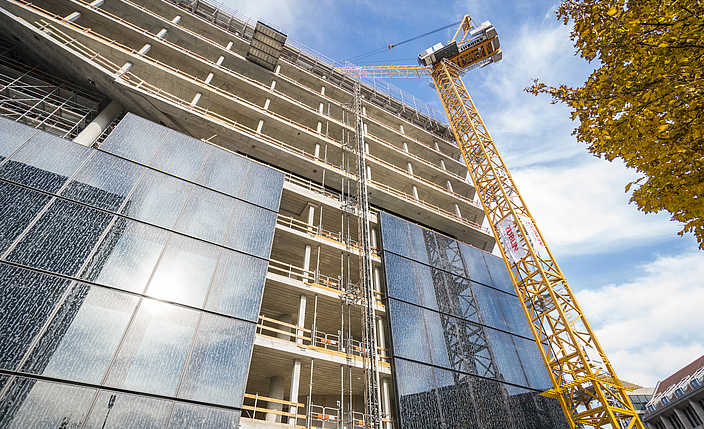 An einem Neubau einer Gebäudefassade werden Baumaßnahmen durchgeführt.
    