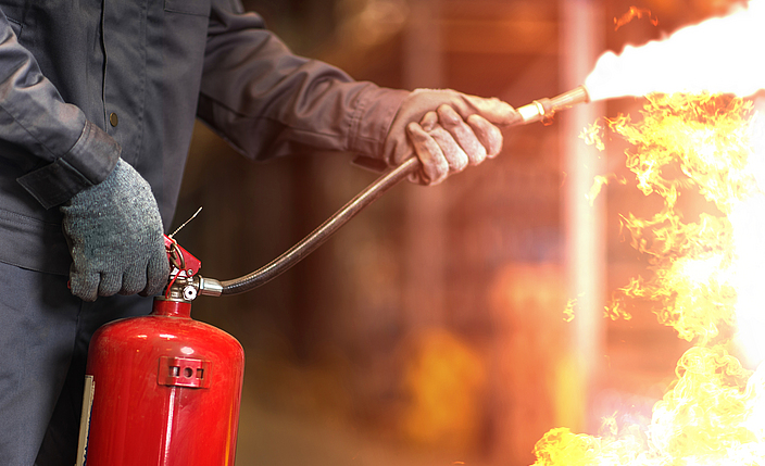 Ein Mann hält einen Feuerlöscher in der Hand und löscht Flammen.
    