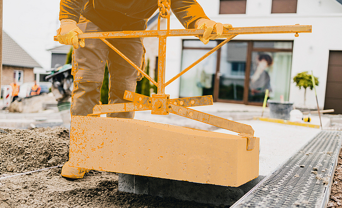 Ein Bauarbeiter hebt mit einer Maschine Betonsteine an.
    